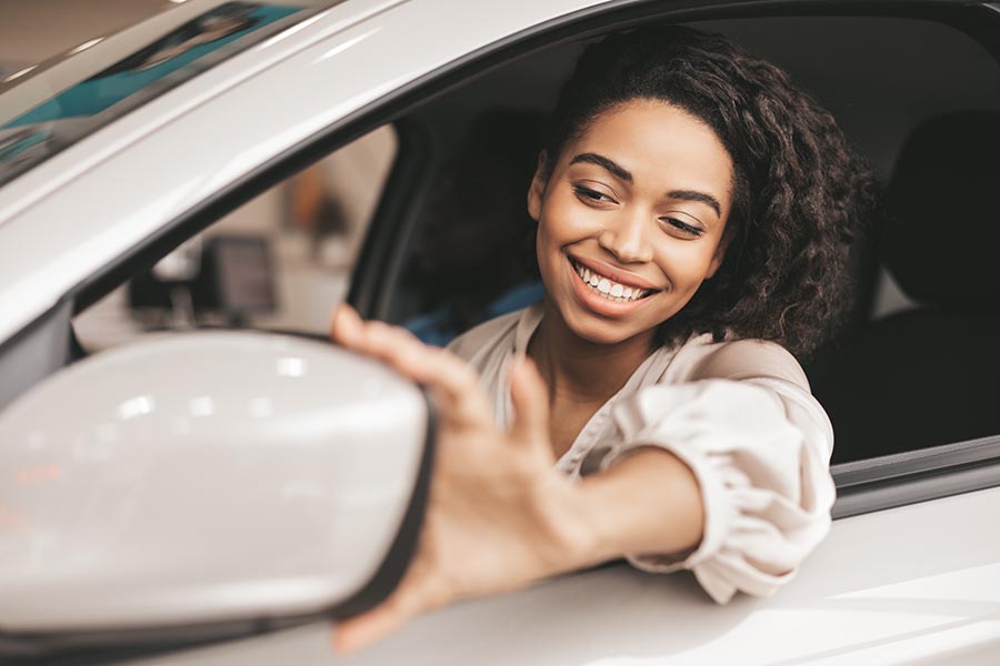 Blog - Woman Adjusting the Mirror on Her White Car, Smiling