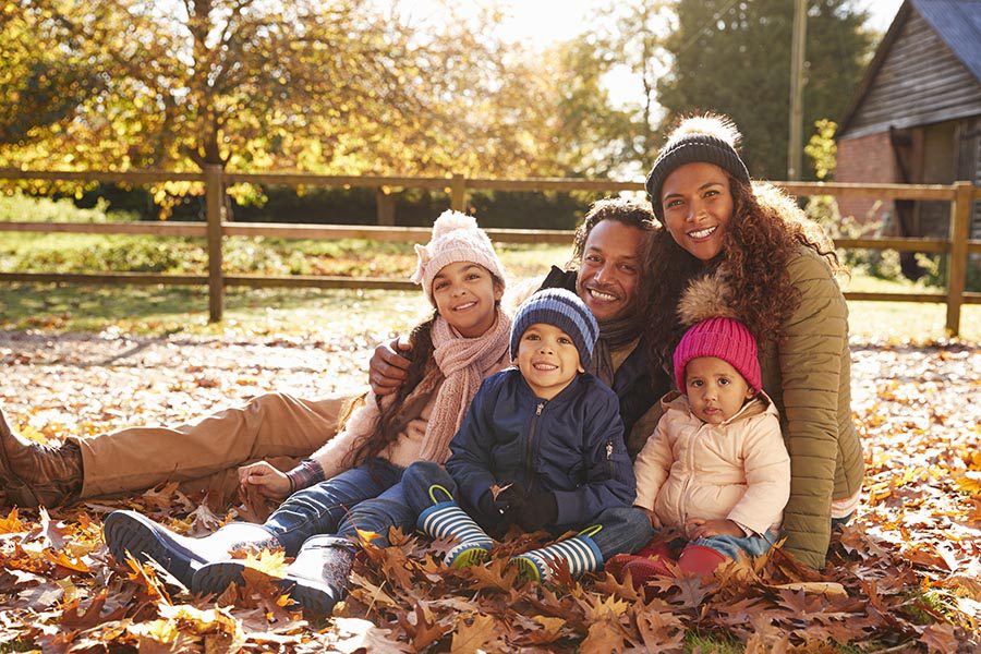 Personal Insurance - Family of Five Sitting in Crisp Fall Leaves in Their Yard, Dressed for Cold Weather