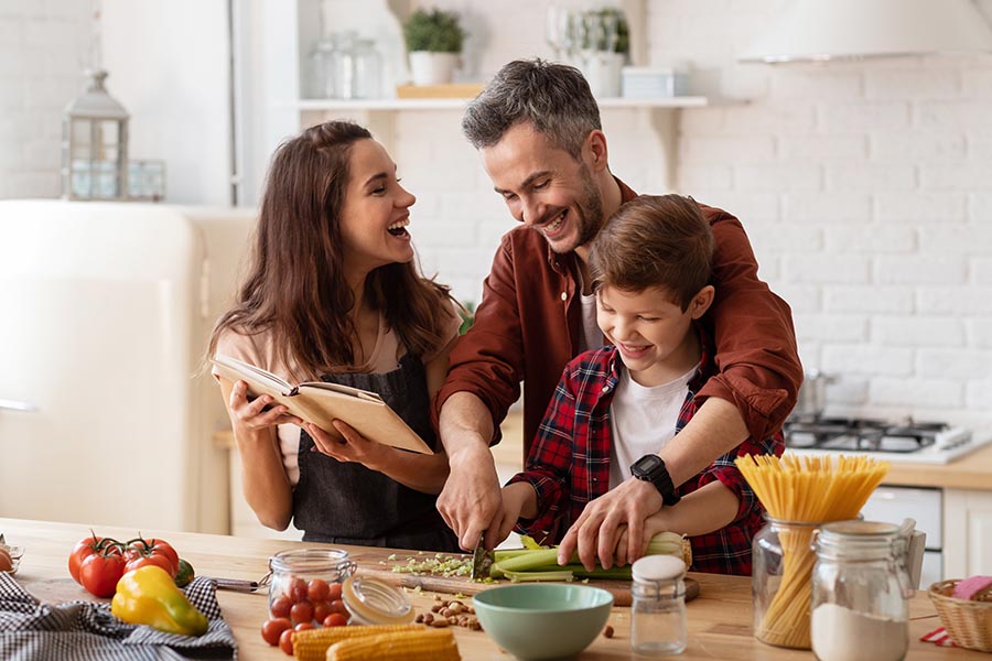 Life and Health Insurance - Family Cooking Dinner Together in Their Kitchen, Laughing and Reading a Recipe Book